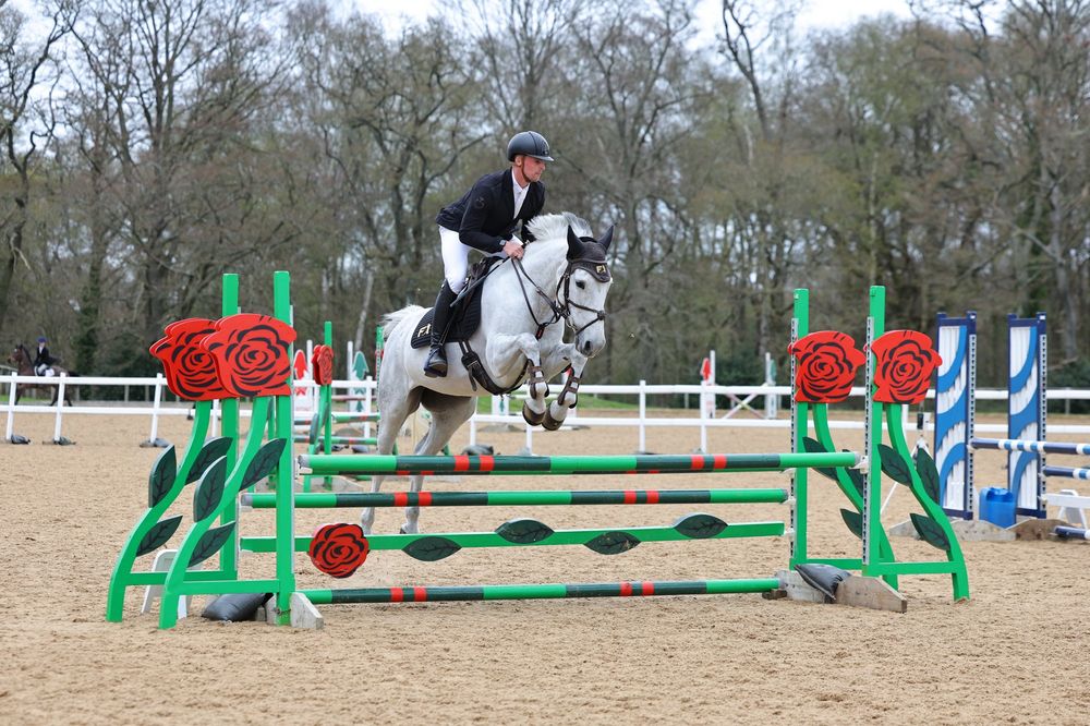 Grey horse and rider clearing a rose-decorated fence