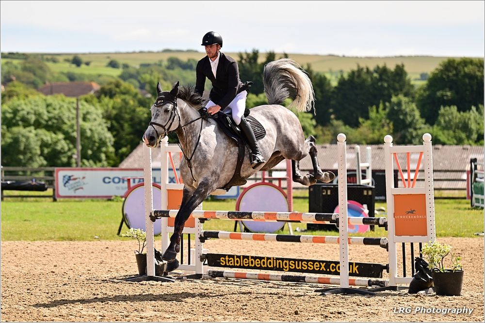 Dappled grey horse jumping a fence in the sunshine